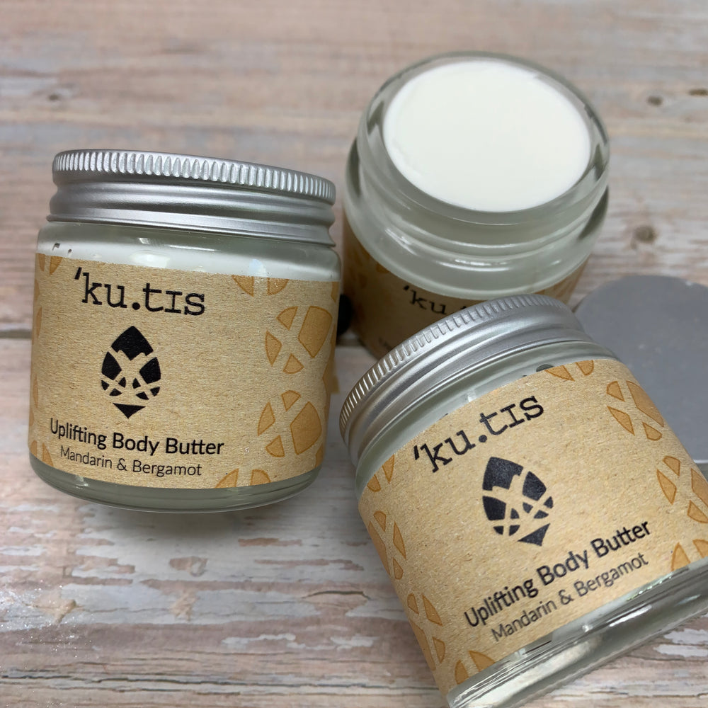 three jars of handmade body butter by kutis, one is open showing a white smooth cream